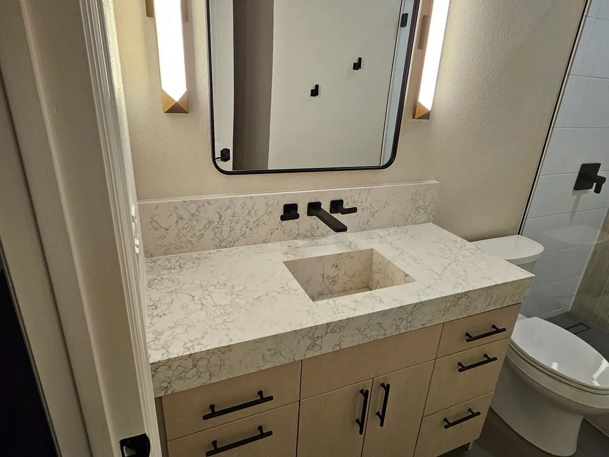 Quartz vanity with black fixtures and lighted mirror