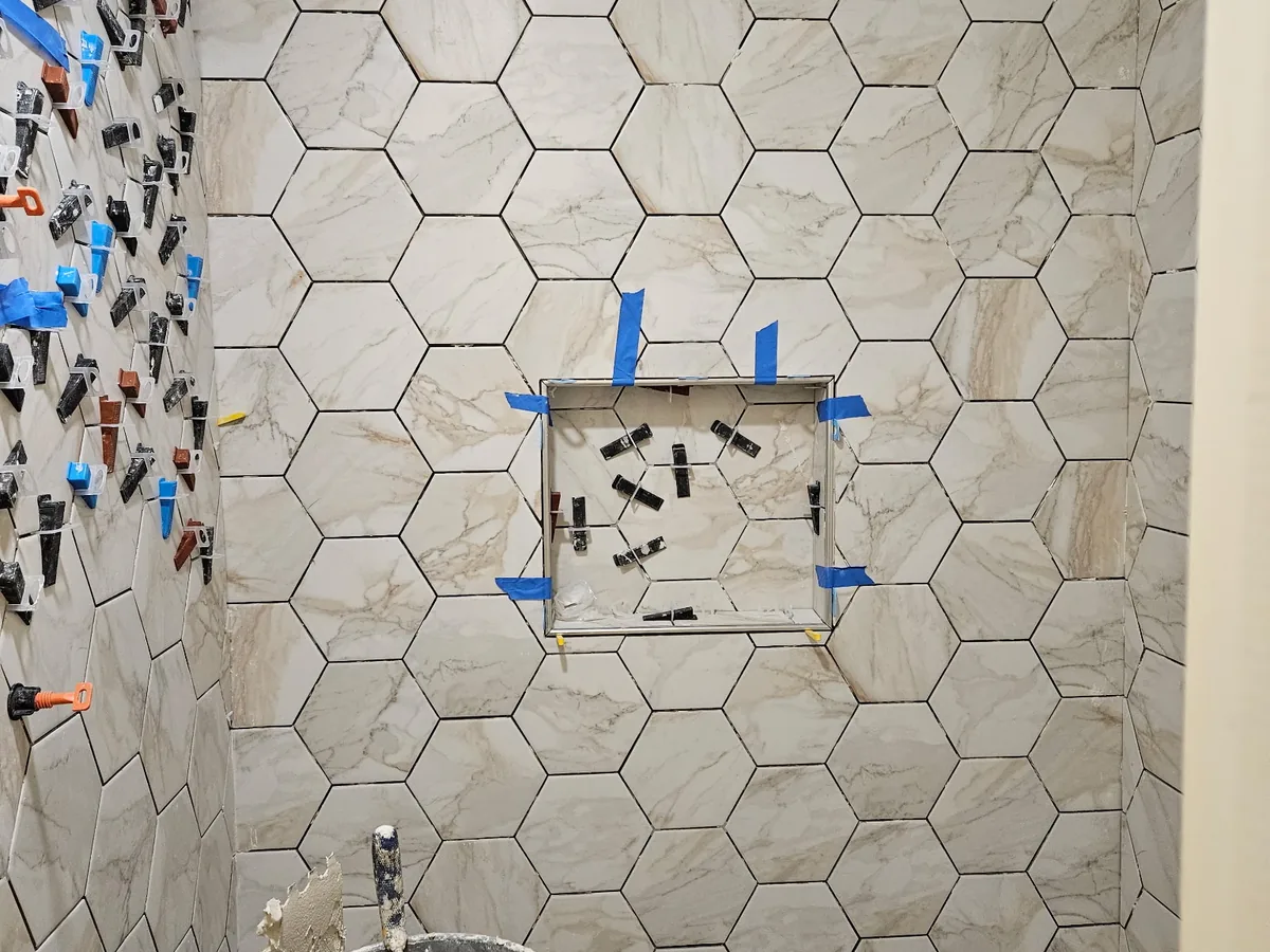 Hexagon marble shower tile installed around a niche